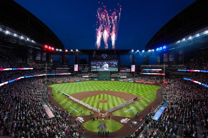 A photo of Chase Field during the National Anthem. Fireworks are going off above the scoreboard. 