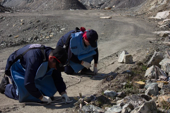 Deminers wearing blue costumes, protections and gloves operating on the field