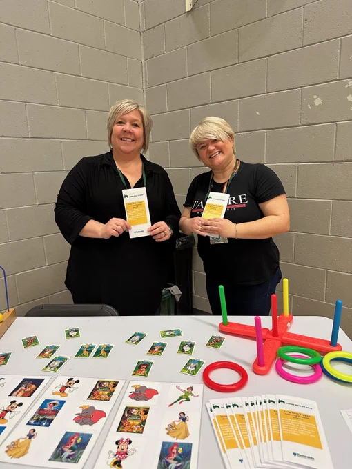 Two people are standing behind a table with promotional materials and a ring toss game. 