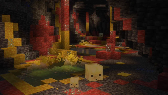 Image of two sulfur cubes curiously looking around in the new Sulfur Cave. Rich reds and yellows color the cave behind them, with a sulfur spring nearby expelling noxious fumes.