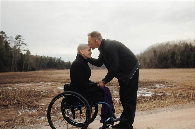 April and Matthew are outside on farmland. Matthew kisses April's forehead.
