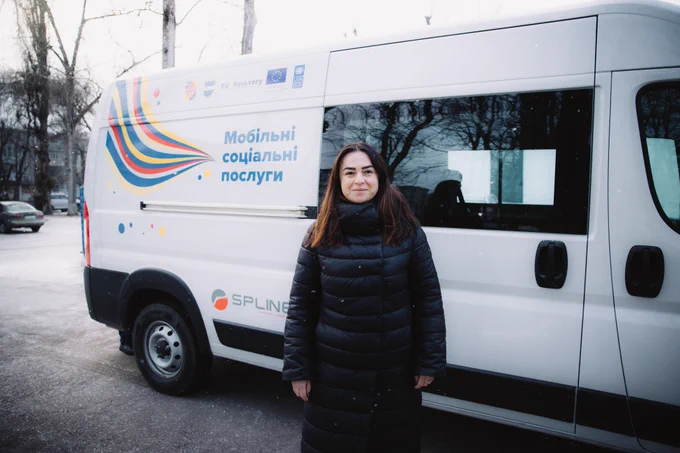 A social worker stands beside a mobile social services vehicle in Kremenchuk, which delivers essential care and support to residents, including older people and those with limited mobility.