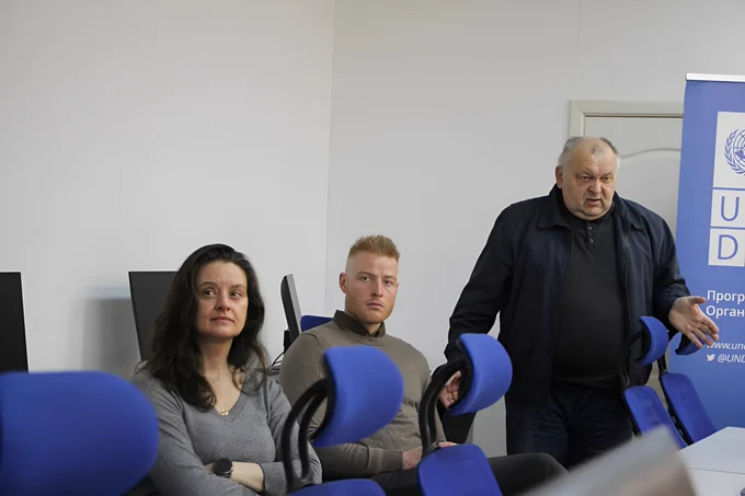 Ana Lukatela (Head of Area-Based Recovery, UNDP in Ukraine) and Jakob Torrild Hansen (Head of the Danish Embassy Office in Mykolaiv),  discuss further cooperation with partner university representatives in Mykolaiv. The setting includes blue office chairs and  UNDP branded banner in the background.