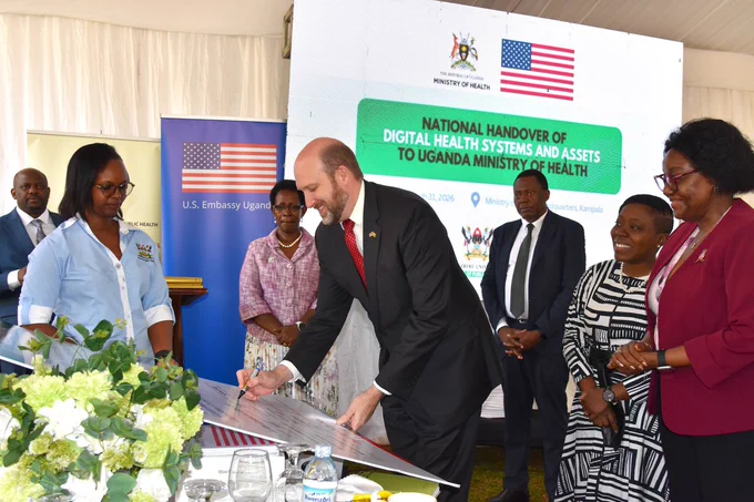 Ambassador Popp signs large board with Ministry of Health and METS staff looking on.