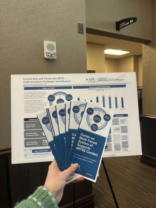 Photo of expert holding MTSS Center brochures in front of a poster session at a conference.