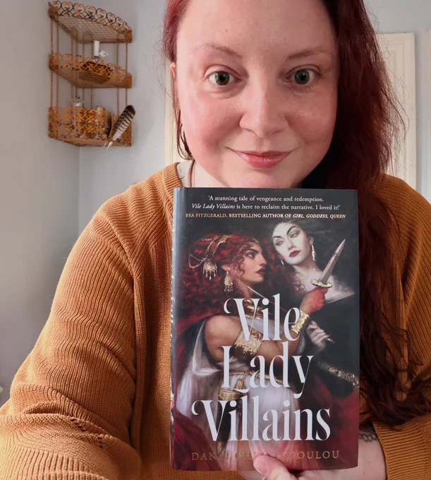 Danai faces the camera holding their book, Vile Lady Villains