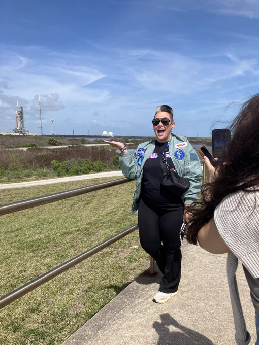 A person poses for a photo with the Artemis II rocket in the background.