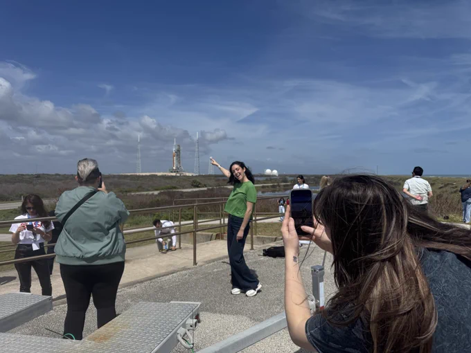 A person poses for a photo with the Artemis II rocket in the background.