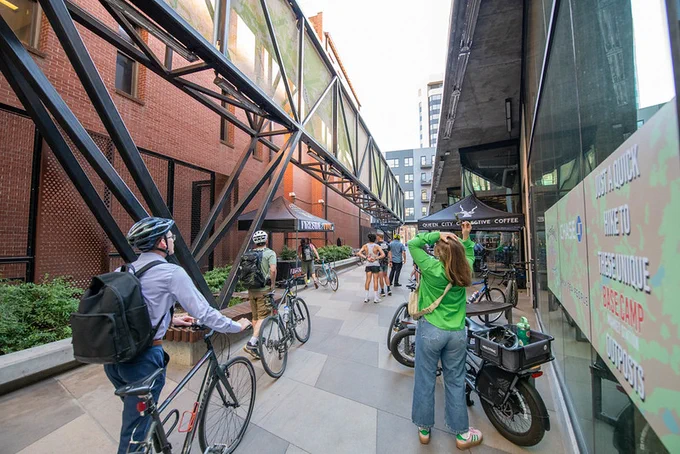 People walk beside their bicycles along a pedestrian path between buildings.