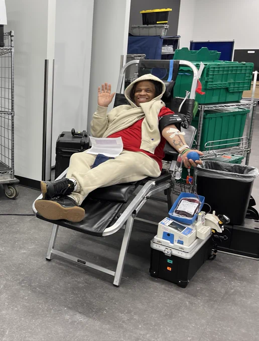 An AES Ohio employee relaxes in a donation chair during a blood drive, holding a stress ball while medical equipment operates nearby.