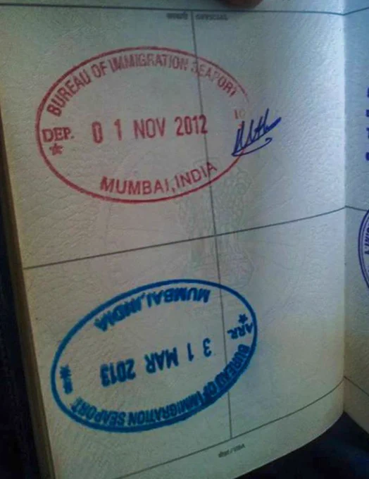 "A close-up, high-detail photo of an official Indian passport page. The blue ink entry stamp from the Mumbai Immigration office at Yellow Gate is visibly printed upside down, dated 01 APR 2013. The weathered paper and the inverted stamp serve as a silent, ironic witness to the return of a solo sailor who had been at sea for five months, rounding Cape Horn to reach the very place he had never technically left