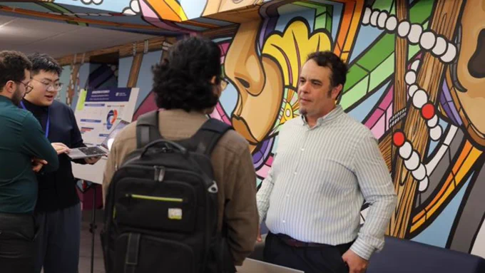 Two people speaking in front of a mural