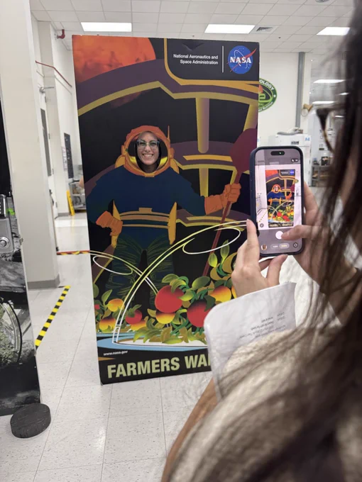 A person uses a mobile phone to take a photo of another person posing with a photo prop inside the plant lab at NASA’s Kennedy Space Center in Florida.