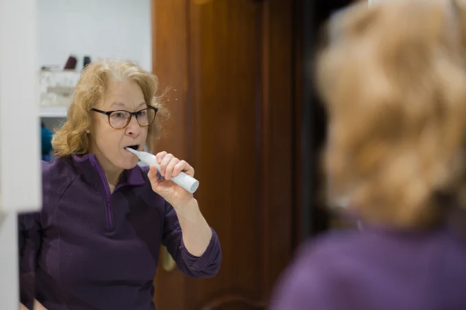 Senior woman brushing teeth with electric toothbrush in bathroom - stock photo
