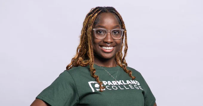 PascalineGrace stands with her hands on her hips in black leggings and a green Parkland College t-shirt.
