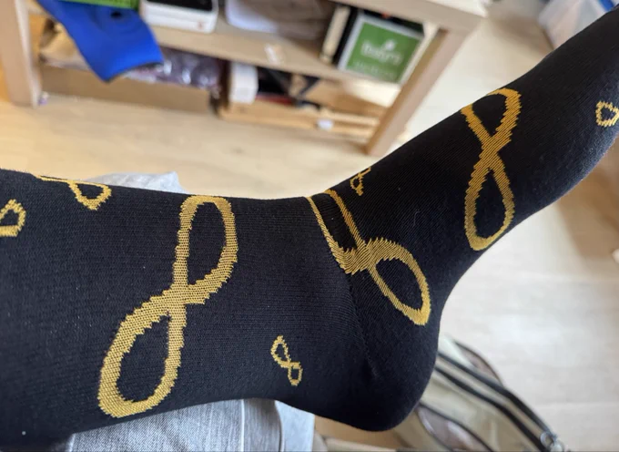 Image of a long foot and bottom of a calf wearing one of the black with autistic infinity symbol (gold) socks from the previous picture. It fits perfectly!