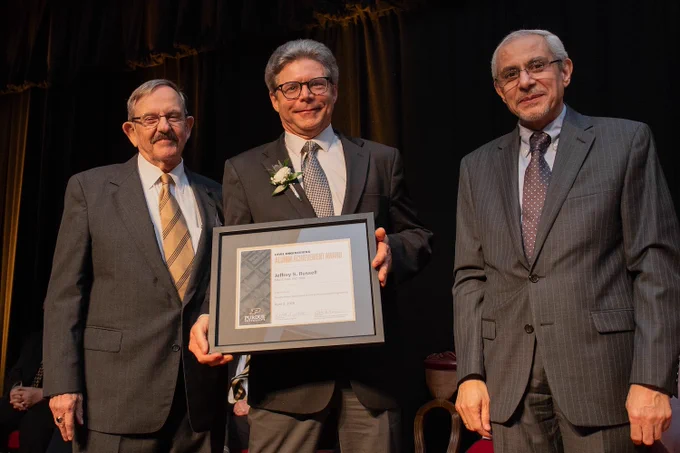 Jeff Russell, UW-Madison Dean of Continuing Education and Professor of Civil and Environmental Engineering smiles and holds a framed certificate.