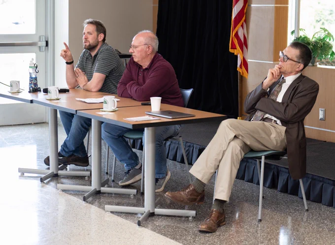 Three men seated at table near stage