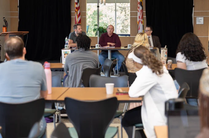Three panelists at front of room with people seated at tables listening