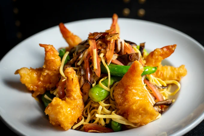 Plated linguine in a large white bowl topped with golden tempura shrimp
