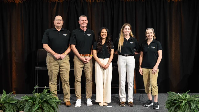 The five-person Purdue 1 crew poses together on stage at the crew announcement event in Neil Armstrong Hall of Engineering. From left to right: Steven Collicott, professor of aerospace engineering; Jason Williamson, Purdue alumnus; Abby Mizzi, Purdue aeronautical and astronautical engineering graduate student; Beth Moses, veteran astronaut and associate professor of engineering practice; and Florence Stivarga, research scientist at AWS. All five wear matching black Purdue 1 "Crew" polo shirts and smile in front of a dark curtain backdrop with fern plants at the base of the stage.