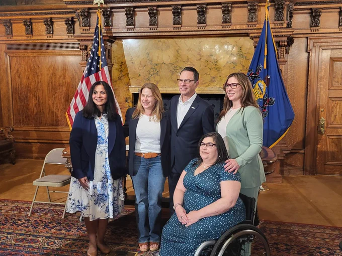 Image of 5 people posing in front of an American flag and a Pennsylvania flag, the individual on the far left is DRP's Director of Public Policy Dale Verchick and at the center is Governor Shapiro, along with three other women. 