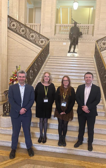 Danny and Peter McReynolds with Sarah and Emily from ADDNI on the staircase in the Great Hall in Parliament Buildings.
