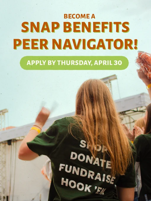 A person with long hair is facing a stage at an outdoor event, with others nearby. They are wearing a dark T-shirt with the words "Shop, Donate, Fundraise" on the back. Text on the image reads, "Become a SNAP Benefits Peer Navigator! Apply by Thursday, April 30.
