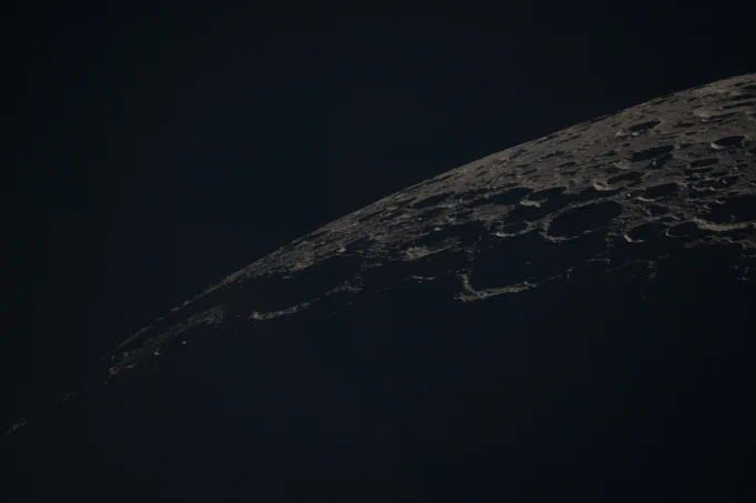 The dimly lit far side of the Moon arcs from the bottom-left to top-right of this image. Its surface is covered in circular craters. Credit: NASA