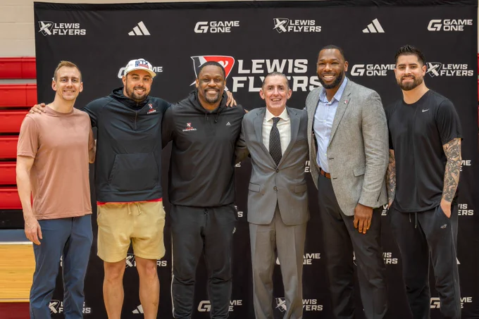 A group of six people stands in front of a backdrop featuring the Lewis Flyers logo. They are in a gymnasium setting, with some individuals wearing athletic attire.
