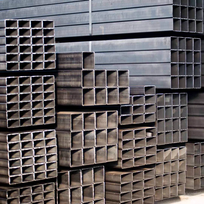 Stacks of hollow rectangular steel tubes piled in rows at an industrial site.
