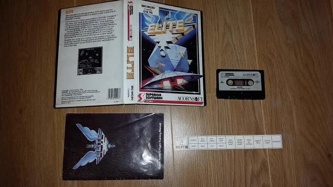 Retail box contents for BBC cassette Elite by Superior Software/Acornsoft (1987). Included are the tape cassette, Space Traders Flight Training manual and a function key legend.