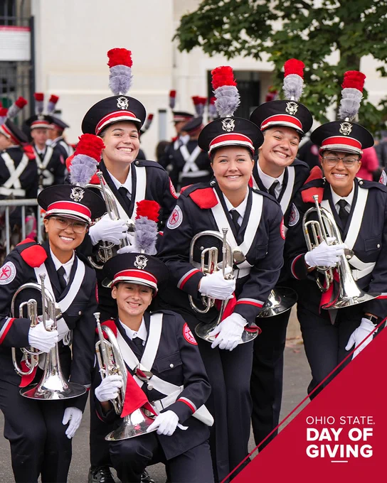 A group of six members of the Ohio State University Marching Band are smiling and posing with their mellophones. They are in uniform with red and gray plumes on their hats. A red, angled banner at the bottom right reads, "Ohio State: Day of Giving.