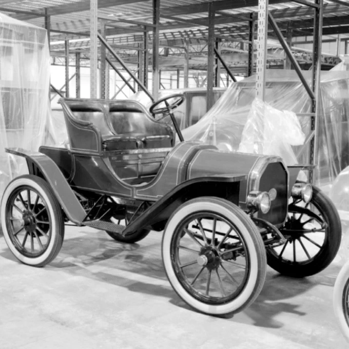 Voiture ancienne du début du XXe siècle avec roues à rayons en bois exposée à l'intérieur d'un entrepôt.