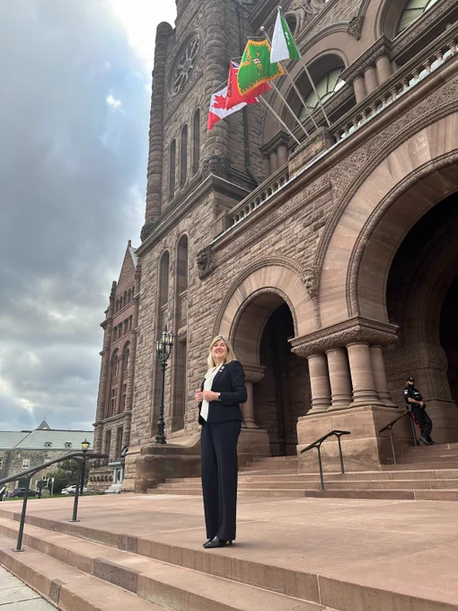 Alison Johnstone on the steps of the Legislative Assembly of Ontario, with flags flying above the entrance.