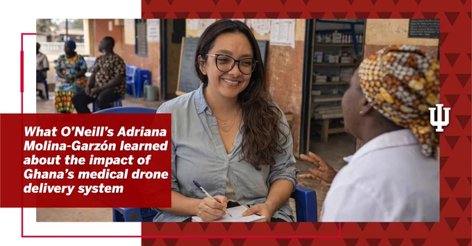Adriana Molina-Garzón is smiling while sitting and taking notes. Another person, wearing patterned clothing and a headscarf, is engaged in conversation with them. The setting appears to be a room with shelves and supplies. A text box reads: "What O’Neill’s Adriana Molina-Garzón learned about the impact of Ghana’s medical drone delivery system," with a red geometric border and the IU trident in the corner.