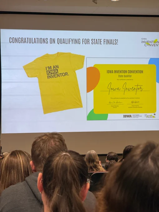 Audience watches a large screen reading “Congratulations on qualifying for state finals!” with an Iowa Invention Convention slide.
