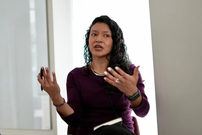 María Piñeros-Leaño in a purple shirt, speaking to an audience with her hands gesturing 