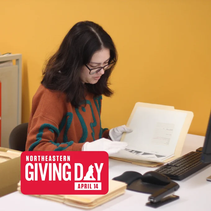 A person sits at a desk wearing white gloves and looking through a file folder of archival materials