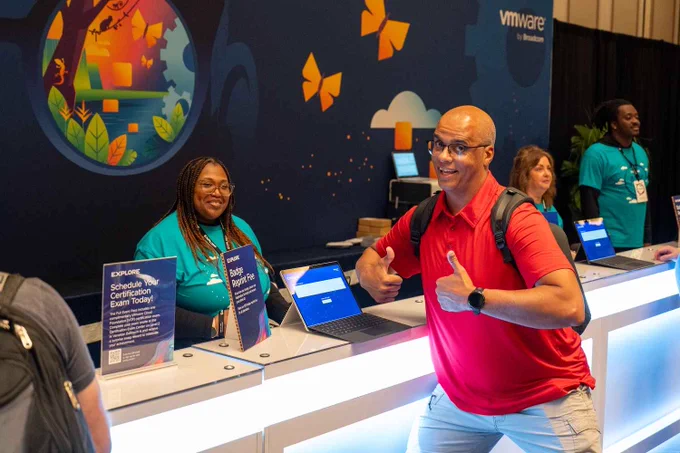 Attendees interact cheerfully at a VMware Explore booth, with informational signs and laptops on the counter.