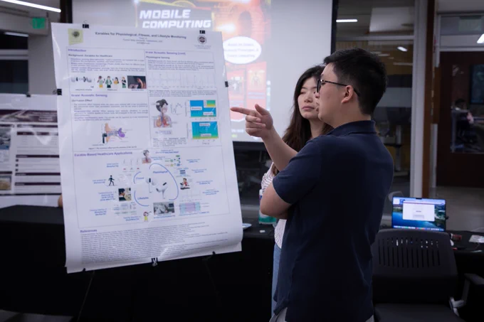 Event photo from the Mobile Computing Demo Showcase. Two attendees stand in front of a research poster.