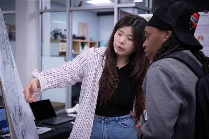 Photo of two attendees conversing in front of a research poster.