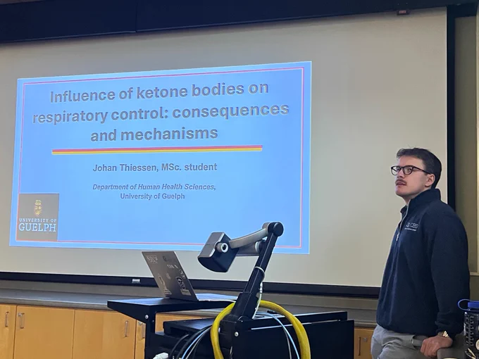 A photo of Johan at his defence, in front of a projected title screen with the same title of his thesis that is listed in this posting.