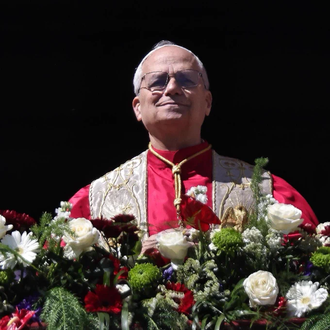 A photo of Pope Leo XIV on a flower-adorned balcony against a vast dark background.