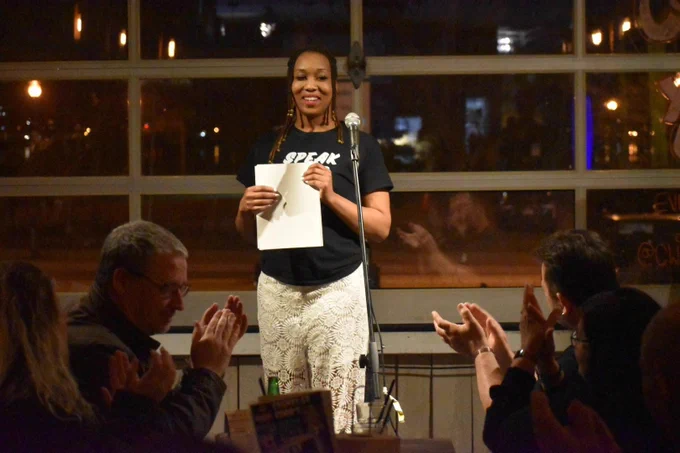 Tyneisha Thomas standing behind a microphone holding papers in front of an audience that is clapping. 