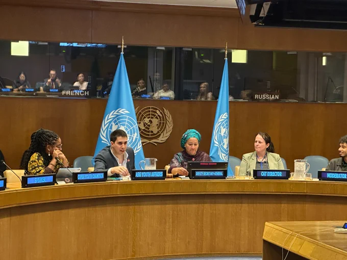 Speakers including ASG for Youth Affairs Felipe Paullier and DSG Amina J Mohammed seated at a United Nations conference table with UN flags and interpreter booths labeled behind them.