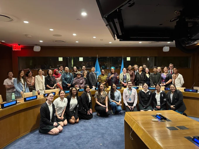 Large group posing in a conference room with blue UN flags behind them, smiling for a group photo.