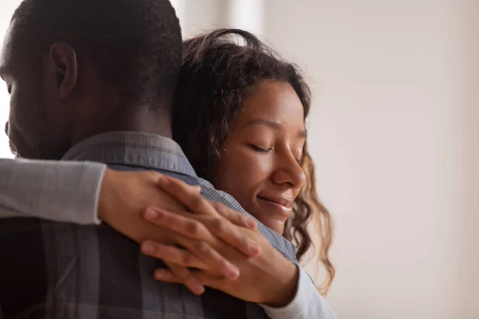 A woman with closed eyes embraces a man warmly, expressing comfort in a close hug
