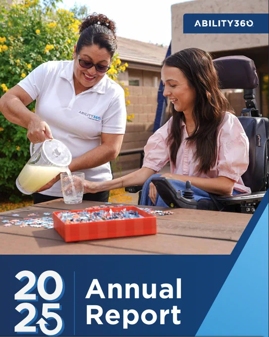 One woman is pouring a glass of lemonade for a woman using a powerchair. they are around a table with a puzzle spread around.