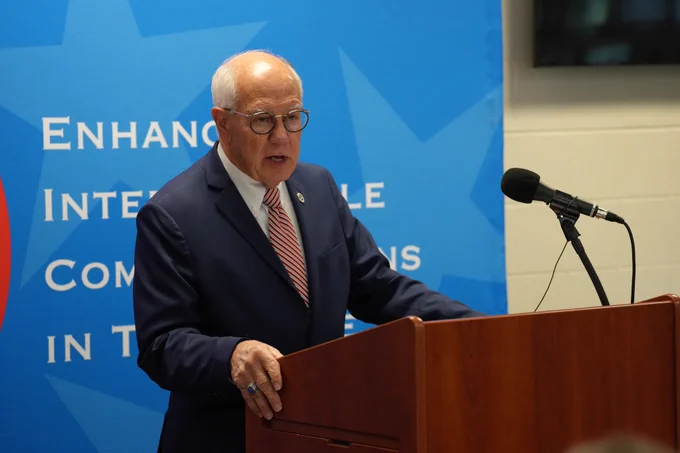 Commissioner Jeff Long speaking at a podium in front of the TACN backdrop.